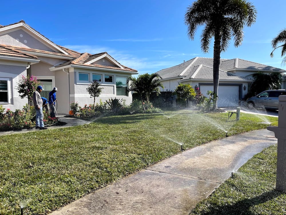 crew working on flower beds and sprinklers going to water lawn